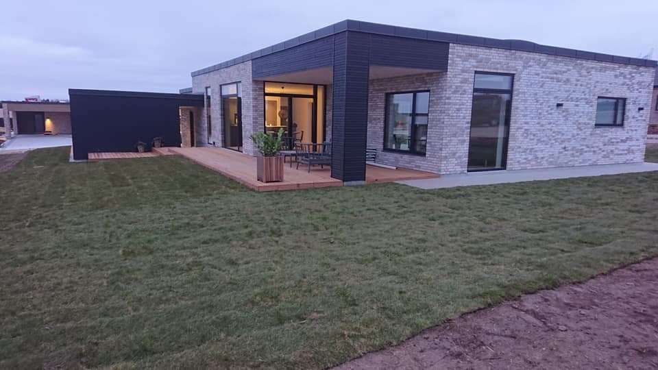 Moderne murstenshus med træterrasse og græsplæne