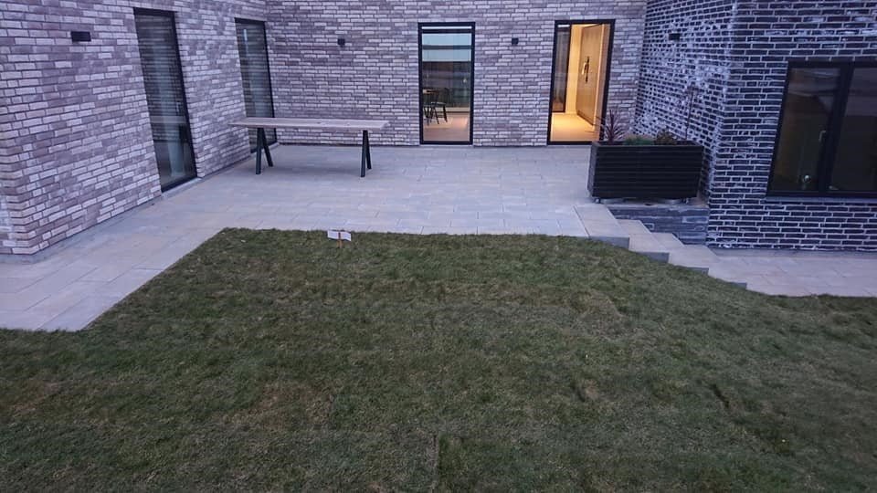 Moderne terrasse med græsplæne og murstenshus